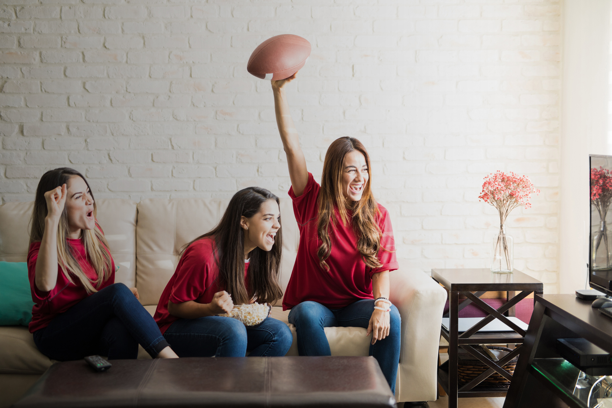 Three roomies wearing team jerseys and watching a football team on tv, celebrating a touchdown